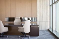 an empty office with two white chairs in front of a wooden desk and large windows