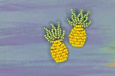 two yellow and green pineapple shaped brooches on a blue wooden background with white beads