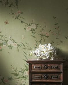 an old dresser with flowers on it in front of a floral wallpaper