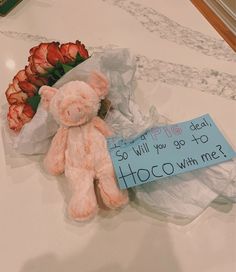 a pink teddy bear sitting next to flowers and a sign that says, i will you go to hoco with me?