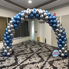 an arch made out of silver and blue balloons is in the middle of a room