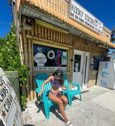 a woman sitting on a blue chair in front of a small building with a sign