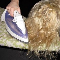 a blonde haired woman ironing her hair with a white and blue steam iron on top of it