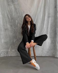 a woman sitting on top of a wooden chair in front of a white backdrop wearing a black suit