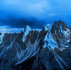 the mountains are covered in snow under a blue sky with dark clouds above them,