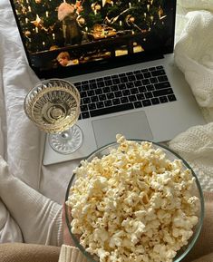 a glass bowl filled with popcorn next to a laptop computer on a bed and blanket