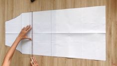 two hands are measuring the length of a piece of paper on a wooden table with scissors