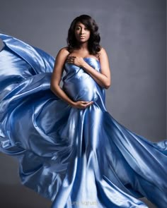 a pregnant woman in a blue gown posing for a photo with her hands on her belly