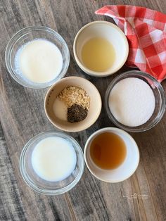 four bowls filled with different types of food on top of a wooden table next to a red and white checkered napkin