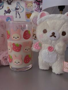 a white teddy bear next to a glass with strawberries on it and other stuffed animals