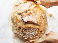 a person holding a loaf of bread wrapped in paper on top of a white surface