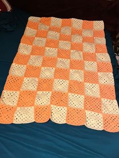 an orange and white crocheted blanket laying on top of a blue bed sheet