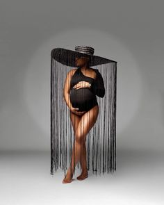 a woman in a black dress and hat standing behind a sheer curtain with her belly exposed