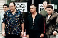 three men standing in front of a store with signs on the door and one man wearing a black shirt