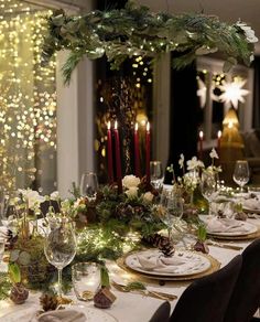 a table set for christmas dinner with candles and greenery in the center, surrounded by festive decorations