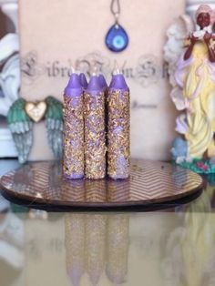 three purple candles sitting on top of a wooden tray next to angel figurines