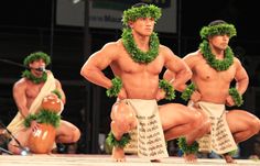 three men in hula skirts and grass wreaths on their heads, one man is squatting down