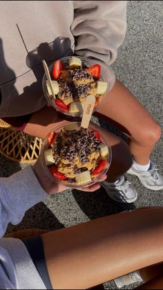 two people holding bowls of food on the ground with their legs crossed in front of them