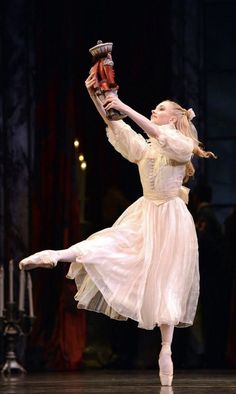 a young ballerina is performing on stage with her arms in the air while holding a pair of red shoes