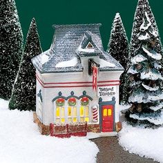 a small white house in the middle of snow covered trees and road with lights on