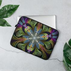 a laptop computer case with a colorful flower design on the front and side, sitting next to a potted plant