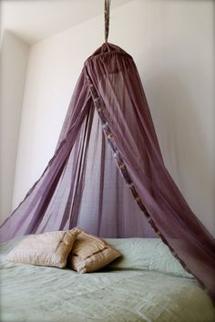 a bed with a purple canopy over it and two pillows on top of the bed