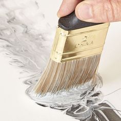 a hand holding a paint brush over a white surface with silver and gold designs on it