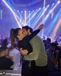 a man and woman kissing in front of a crowd at a concert with bright lights