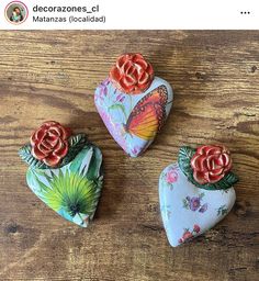 three heart shaped stones with flowers and butterflies on them sitting on a wooden table next to each other