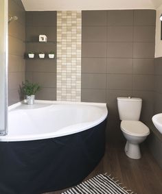 a white toilet sitting next to a bath tub in a bathroom on top of a hard wood floor