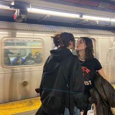 two people are standing in front of a subway train and kissing on the nose while another person stands next to them