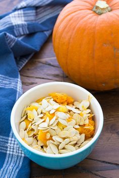 a bowl filled with oats and pumpkins next to a blue towel on a wooden table