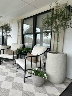 two white chairs sitting on top of a checkered rug next to potted plants