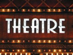 the words theatre are lit up in front of an ornate wooden sign with lights on it