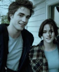 two young people standing next to each other in front of a white house with trees