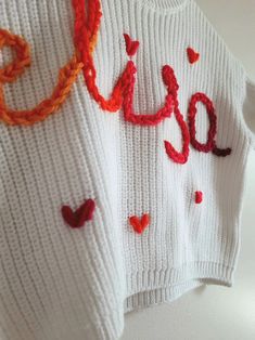 a white sweater with the word love written in red and orange thread on it's chest