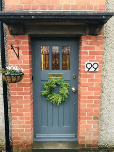 a blue front door with a wreath and number hanging on the brick wall next to it