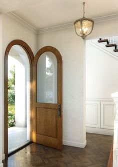 an empty entryway with two arched wooden doors and a light fixture hanging from the ceiling