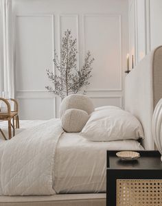 a bed with white sheets and pillows next to a table with a vase on it