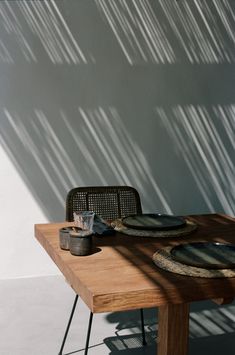 a wooden table topped with plates next to a metal chair under a shadow filled wall