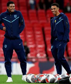 two soccer players standing next to each other on a field with balls in front of them