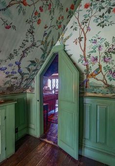 an open door in the corner of a room with floral wallpaper and green cupboards