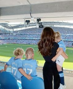 two women and three children sitting in blue chairs at a soccer game with the crowd watching