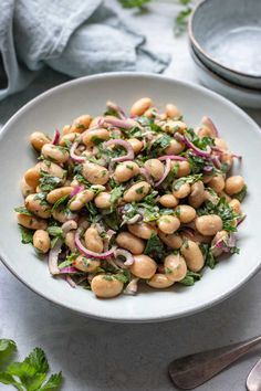 a white bowl filled with chickpeas, onions and cilantro on top of a table