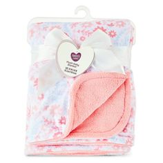 a pink and white blanket with a heart shaped tag on the front, sitting in a package