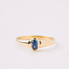 a yellow gold ring with a blue stone on the front and side, sitting on a white surface