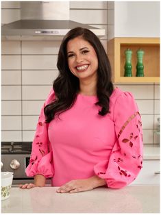 a woman standing in front of a kitchen counter with a cup on it and smiling at the camera