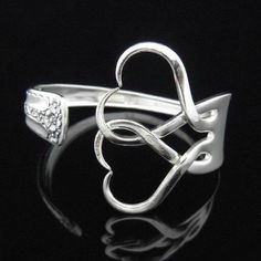 a silver ring with an open heart and two hearts on it's sides, sitting on a black surface