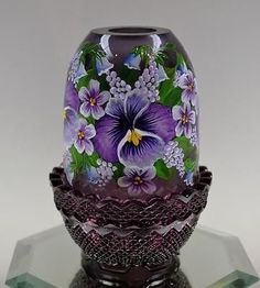 a purple glass vase sitting on top of a crystal base with flowers painted on it