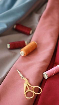 a pair of scissors and some thread sitting on a red cloth with other sewing supplies